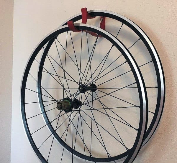 A simple wall-mounted rack holds two bicycle wheels neatly, providing an efficient and compact storage solution for spare parts.