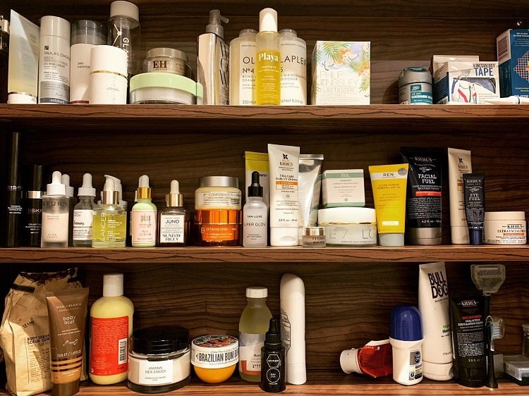 Wooden bathroom shelf filled with various skincare and toiletries products.
