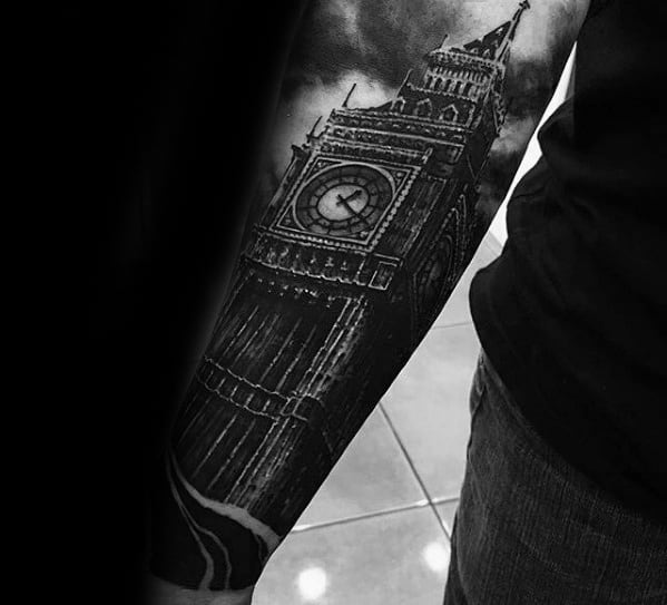 Detailed black and grey tattoo of Big Ben with intricate shading, featuring a dramatic cloudy sky background and clock face prominently displayed on the forearm.