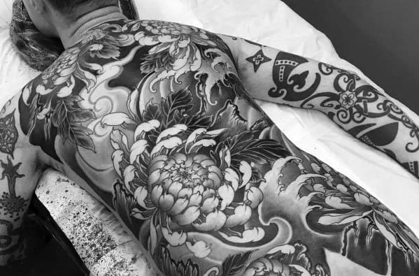 Large full-back tattoo in black and grey featuring intricate peony flowers, swirling wind patterns, and traditional Japanese-style elements.