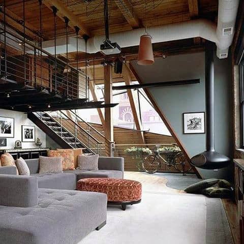 Industrial-style loft living room with gray sectional, fireplace, and large windows.