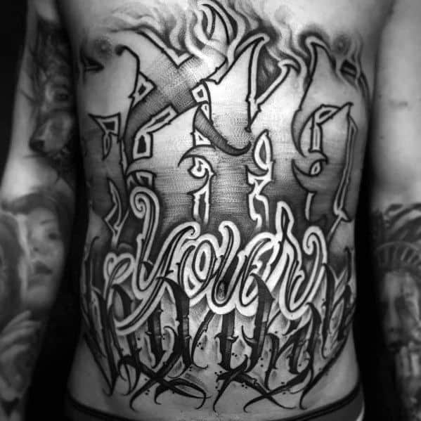 Black and grey full-torso tattoo featuring bold graffiti-style lettering with intricate shading, flames, and abstract elements for a striking look.