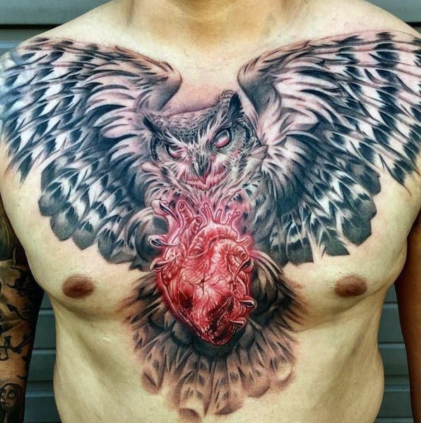Vibrant full-chest tattoo featuring a fierce owl with outstretched wings clutching a realistic, detailed human heart, blending black and grey with bold red.