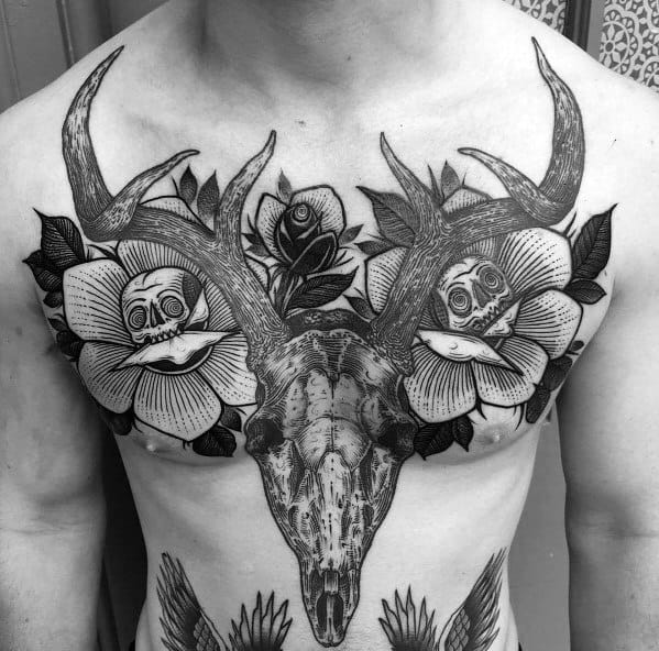 Black and grey chest tattoo featuring a detailed deer skull with large antlers, surrounded by flowers with hidden skulls for a bold and intricate design.