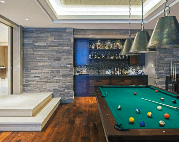 Contemporary billiard room with green felt pool table, stone accent wall, and built-in luxury bar.