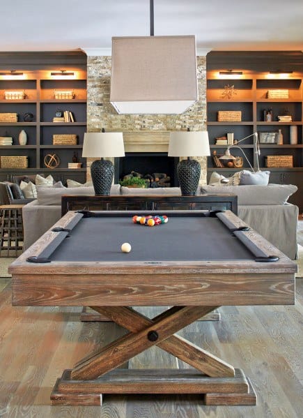 Farmhouse billiard room with a wooden pool table, stone fireplace, and built-in illuminated shelves.