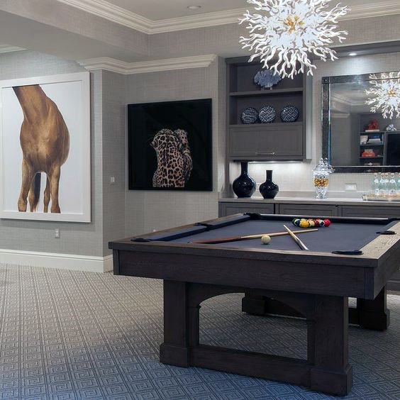 Contemporary billiard room with dark wood pool table, unique chandelier, and modern artwork.