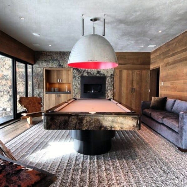 Modern billiard room with unique stone pool table, fireplace, and oversized pendant light.