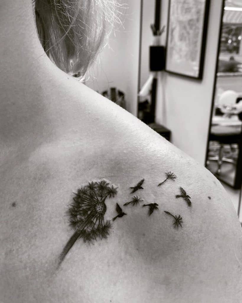 A black and white tattoo of a dandelion with seeds blowing away, transforming into birds. It beautifully represents freedom and change.