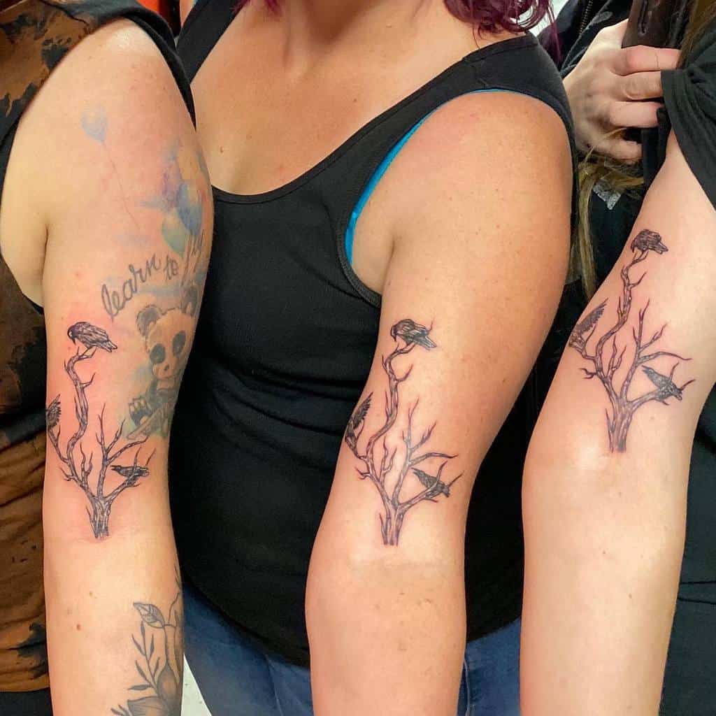 Matching sister tattoos featuring a leafless tree with perched crows, symbolizing strength, connection, and shared history