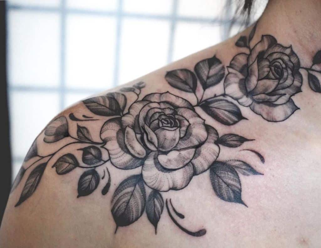 A stunning tattoo of two detailed black and gray roses gracefully adorns the shoulder, with delicate leaves accentuating its beauty
