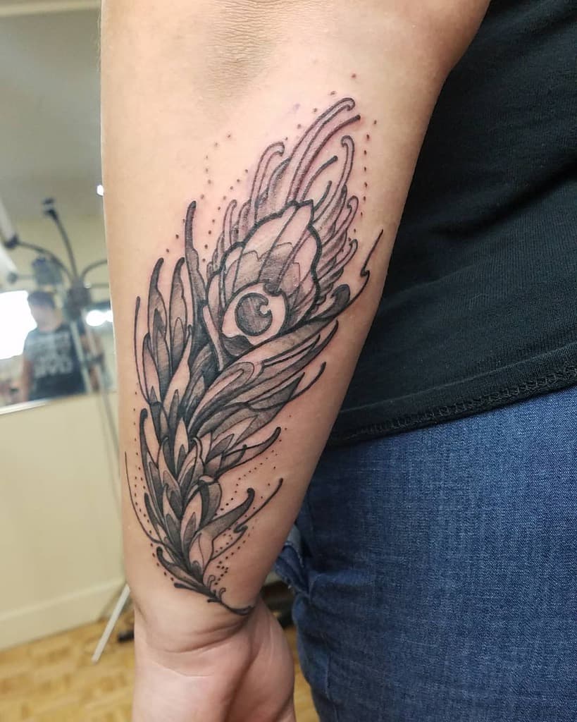 Black and grey peacock feather tattoo on the forearm, featuring bold linework, intricate shading, and decorative dot accents for a unique look.