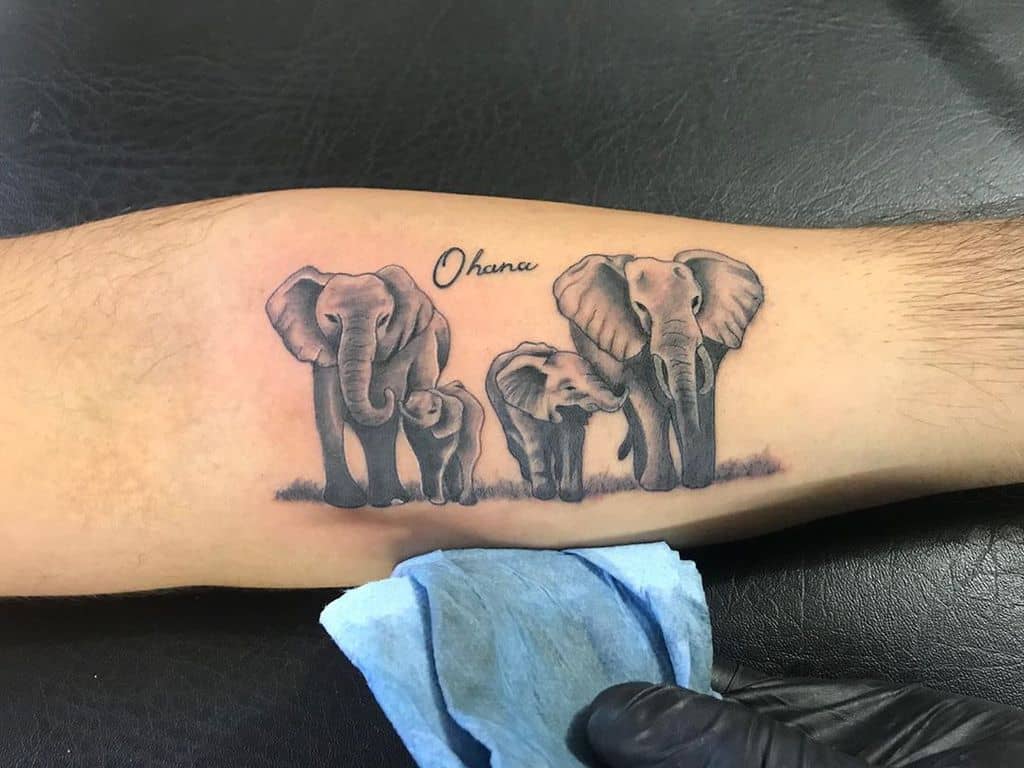 Black and grey elephant family tattoo with 'Ohana' written above, symbolizing family and unity, placed on the forearm.