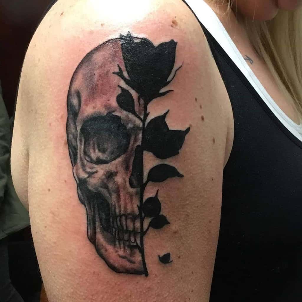 Black and grey tattoo of a half-skull merging into a rose stem, symbolizing life and death with bold shading and contrast on the upper arm.