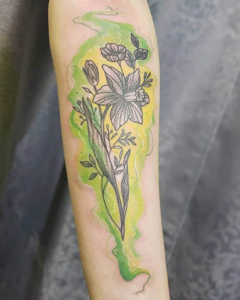 A tattoo featuring a daffodil and other delicate flowers, outlined in black with soft green and yellow watercolor-like accents, creating a vibrant and fresh look.