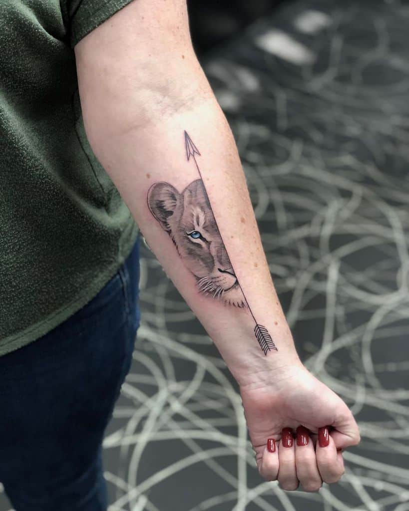 Forearm tattoo featuring a half lioness face with realistic shading, split by a bold black arrow running along the arm for a striking design.