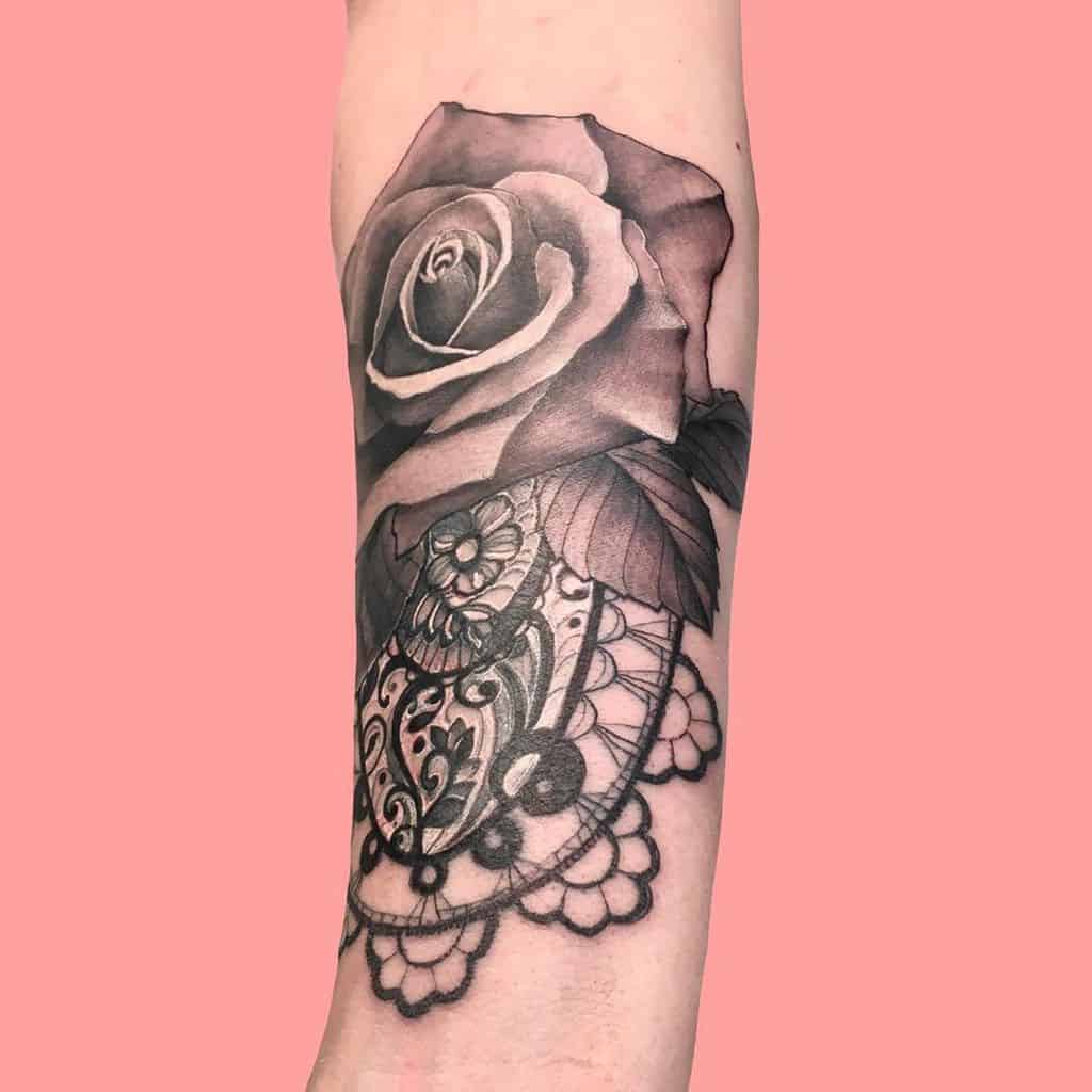 Black and grey tattoo of a realistic rose with intricate lace and filigree details, blending floral elegance with ornamental patterns.