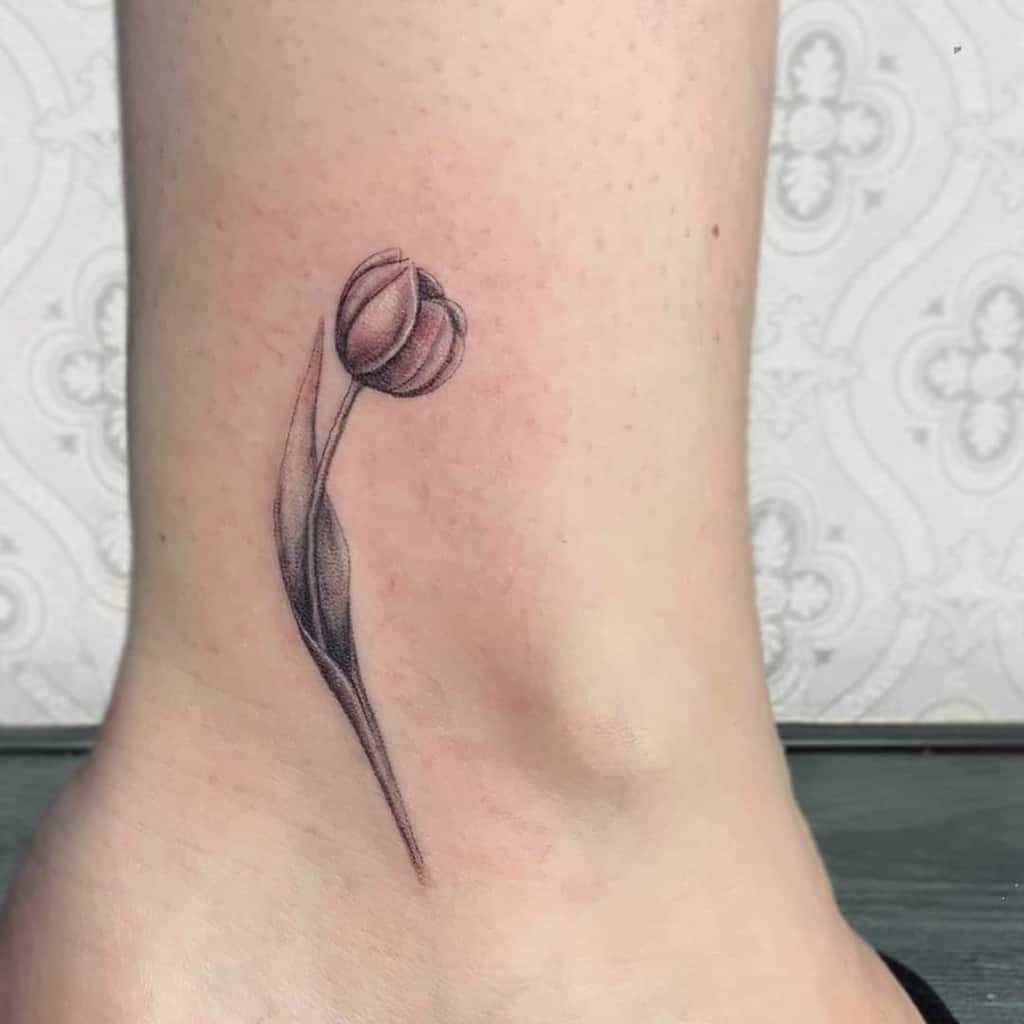 A shaded, realistic tulip tattoo on the ankle with a delicate stem and closed flower, capturing soft details and depth.