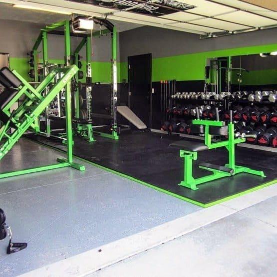 Garage gym with green workout equipment, dumbbell rack, and modern black-and-green decor.