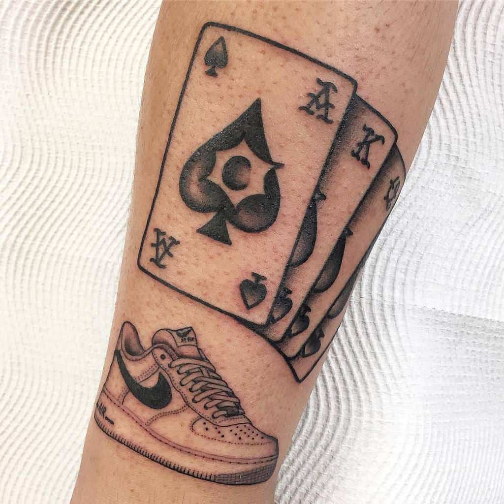 A black-and-white tattoo featuring the Ace, King and Queen of Spades card, alongside a detailed Air Force 1 sneaker