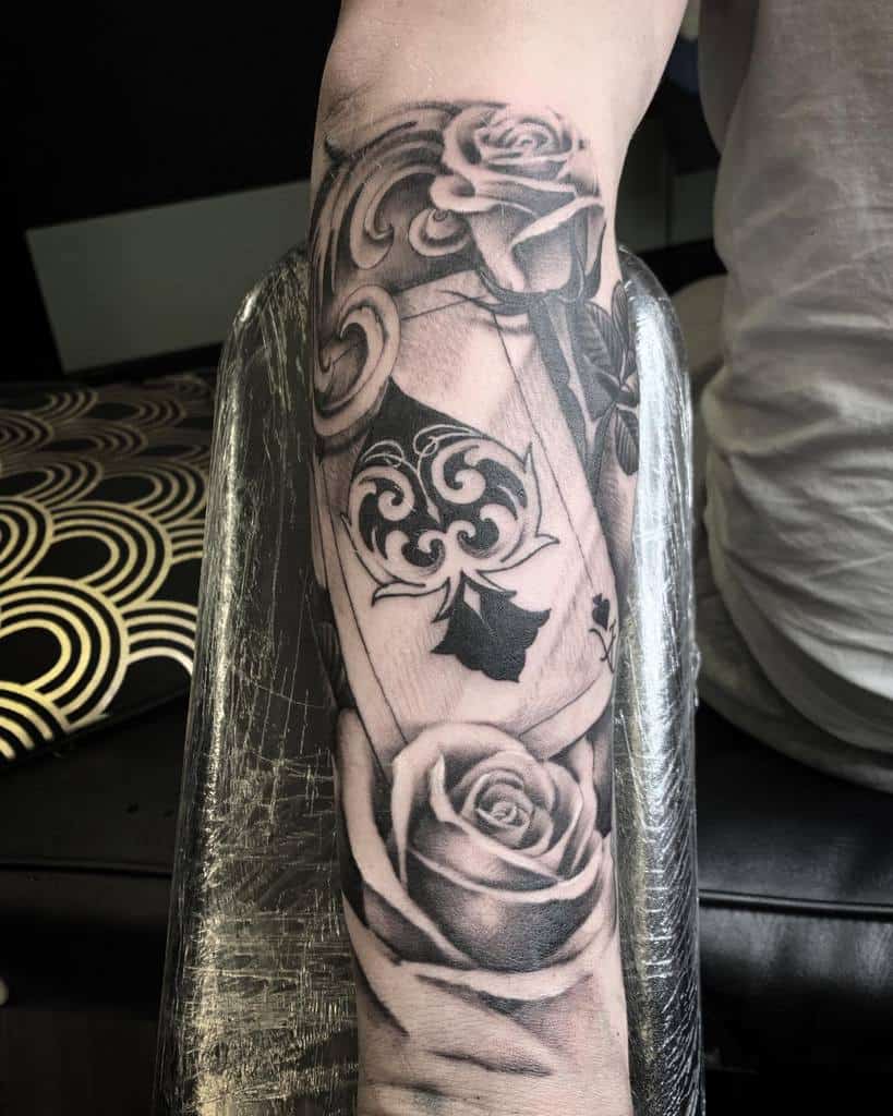 A black-and-white tattoo of an Ace of Spades surrounded by roses and intricate tribal swirls