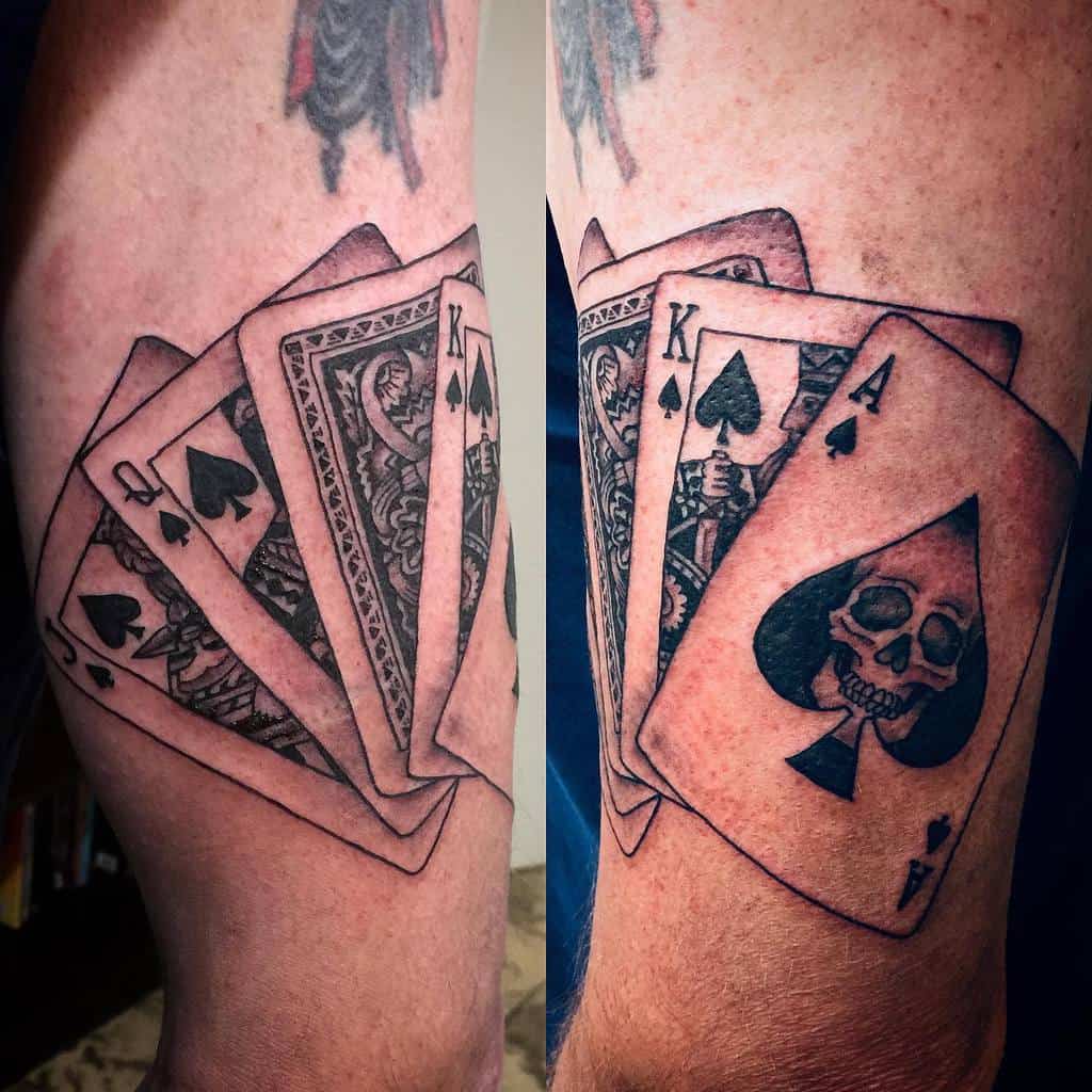 A black-and-white tattoo featuring playing cards with skull in Ace of Spade, including the Ace, Queen, Jack and King of Spades