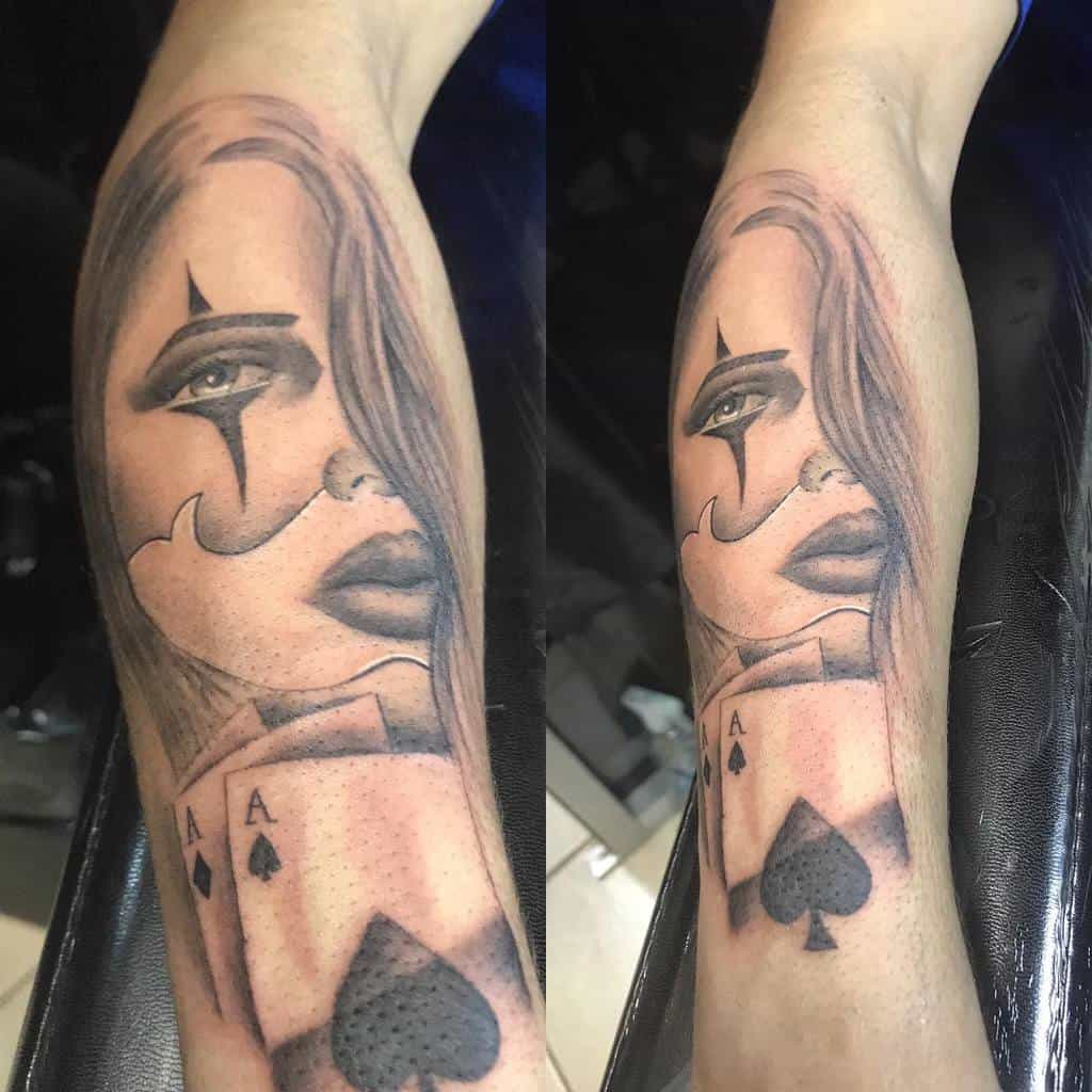 A black-and-white tattoo featuring a woman's face with upper mask, combined with the Ace of Spades card