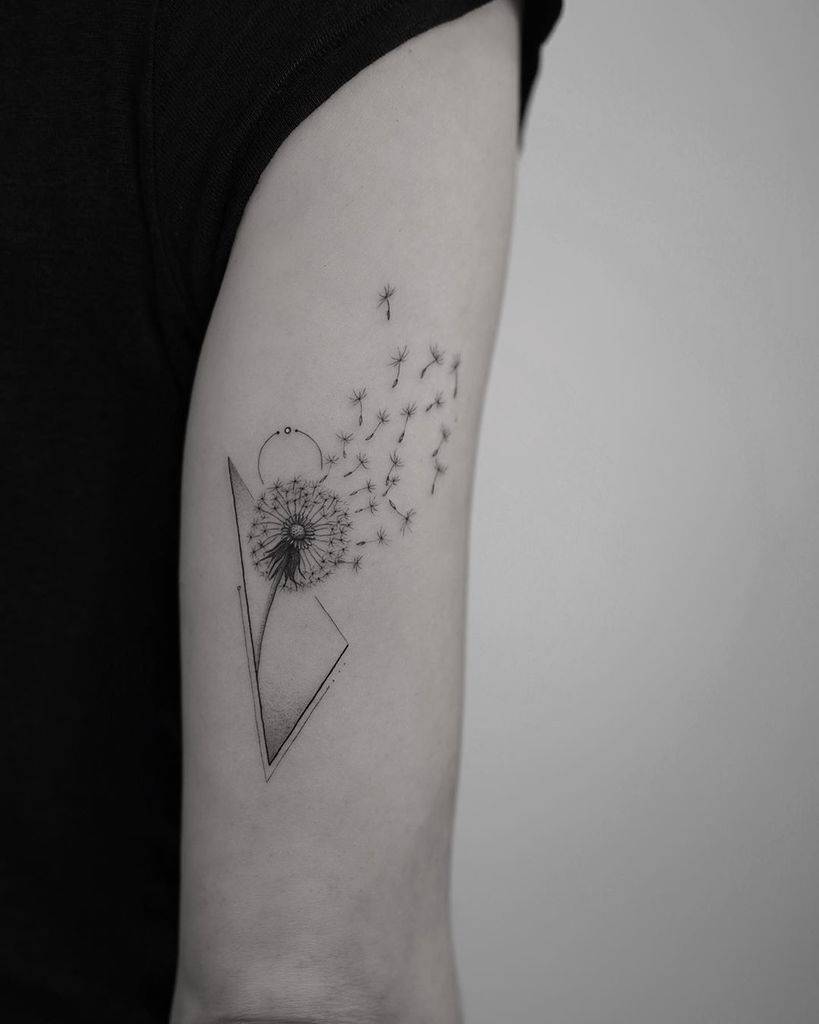 This tattoo features a geometric design with a dandelion at the center, its seeds drifting away in an elegant and abstract pattern. The clean lines and minimalistic style create a modern yet delicate look.