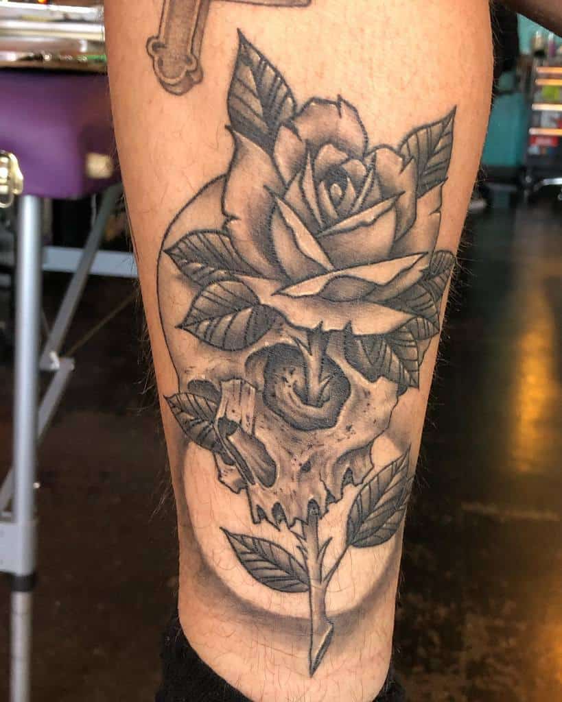 Black and grey tattoo of a skull transforming into a blooming rose, featuring fine shading and intricate details on the lower leg.