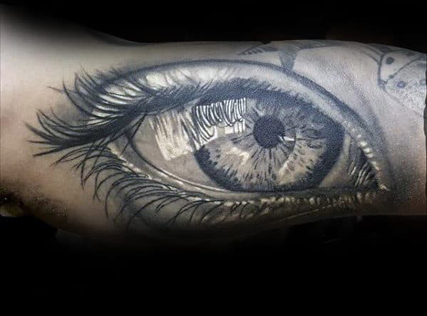Black and white tattoo of a realistic eye with detailed lashes and shading on an arm