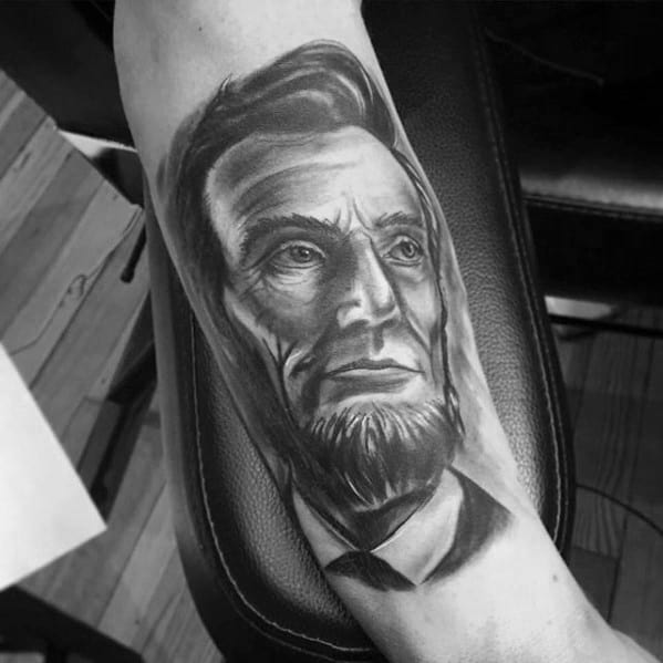 Black and gray tattoo of Abraham Lincoln's bearded face on a person's arm