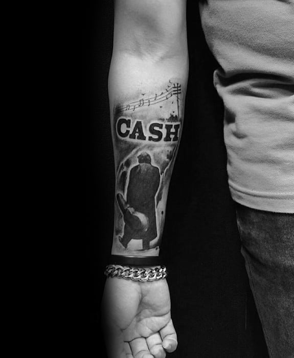 Forearm tattoo with "CASH," Johnny Cash with a guitar, and musical notes