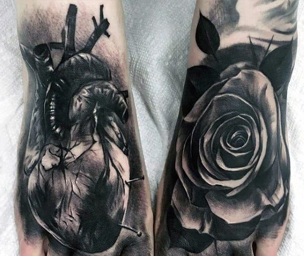 Black and grey 3D tattoos on both hands, featuring a realistic anatomical heart with nails and a detailed rose, symbolizing pain and beauty.
