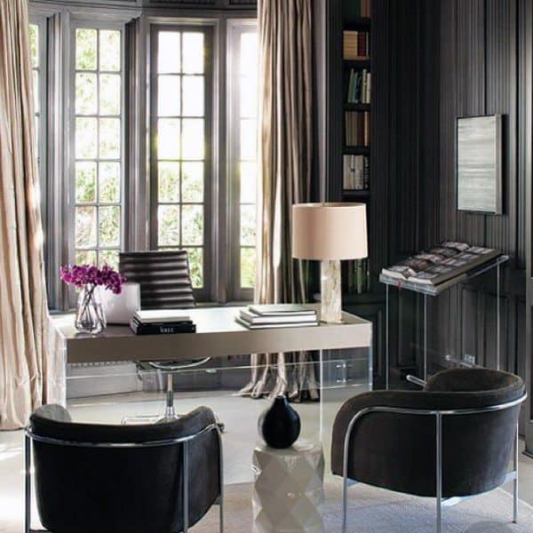 Modern home office with grey tones, glass desk, large windows, and elegant chairs.