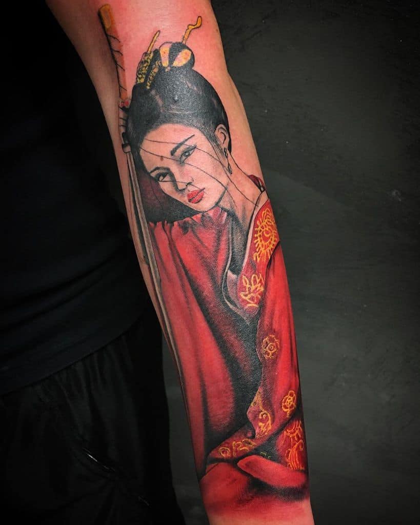 Forearm tattoo of a Geisha in a flowing red kimono with gold details, featuring delicate shading and a striking, expressive gaze.