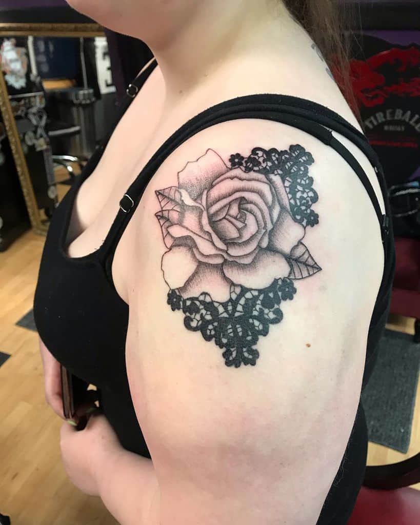 Black and grey shoulder tattoo featuring a detailed rose with delicate lace accents, blending floral elegance with ornamental design.