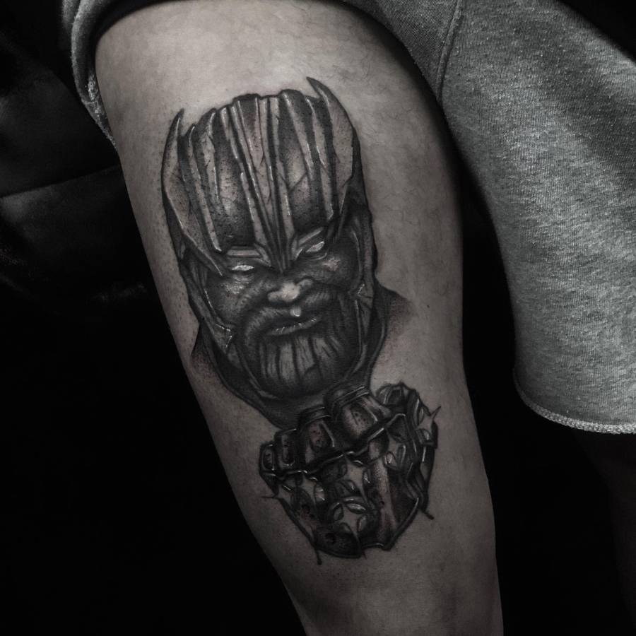 A black and gray tattoo of Thanos with an intense expression, featuring his face and the gauntlet with the Infinity Stones