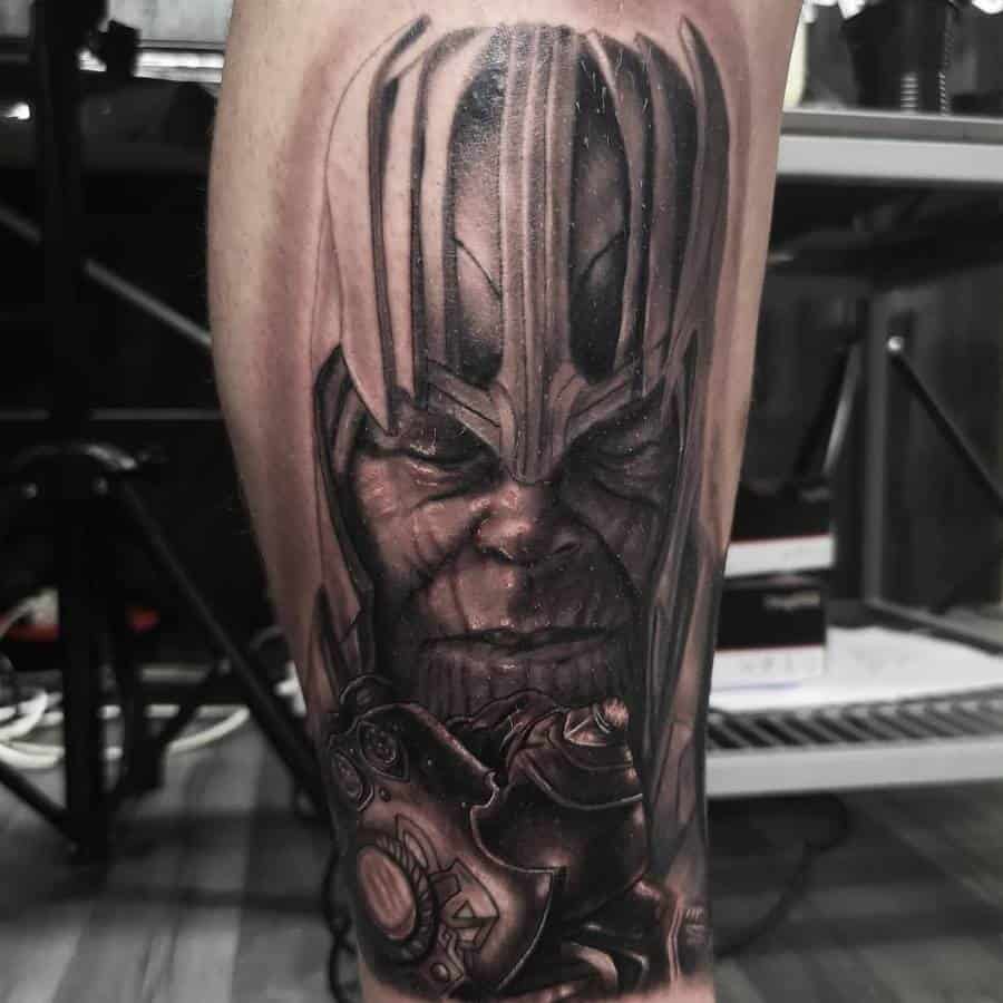 A detailed black and gray tattoo of Thanos' face with the gauntlet on his arm, showcasing sharp features and intense shading