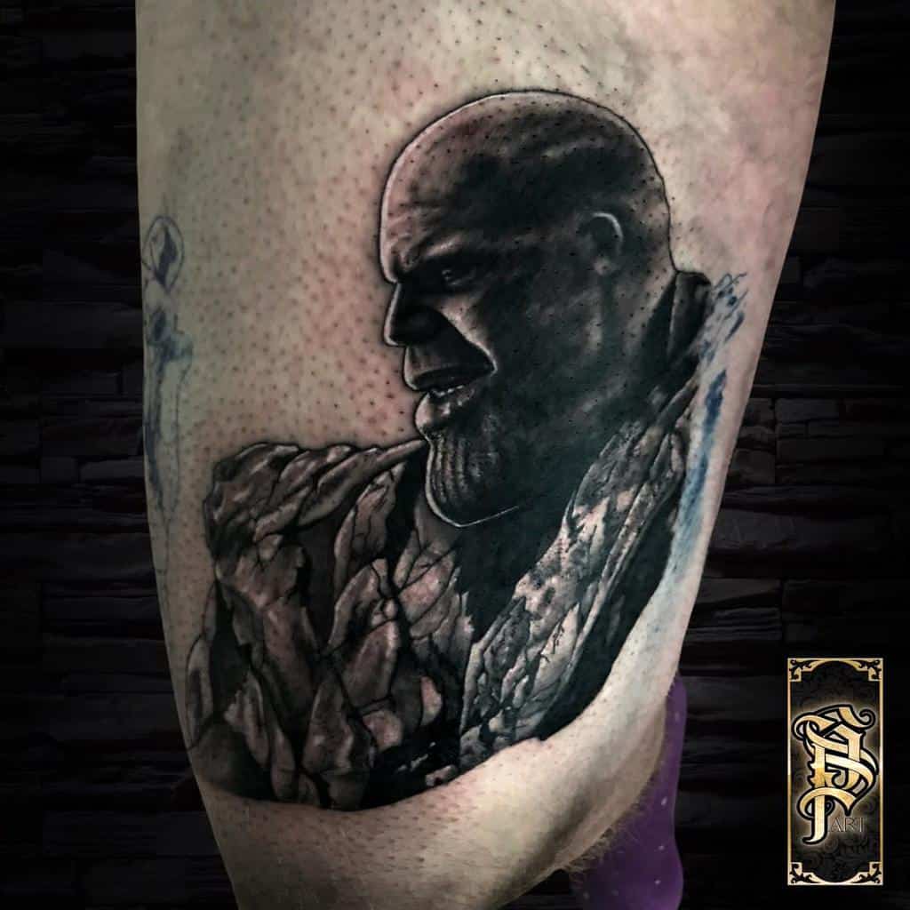 A black and gray tattoo of Thanos, showing his side profile with detailed shading and a cracked rock-like texture