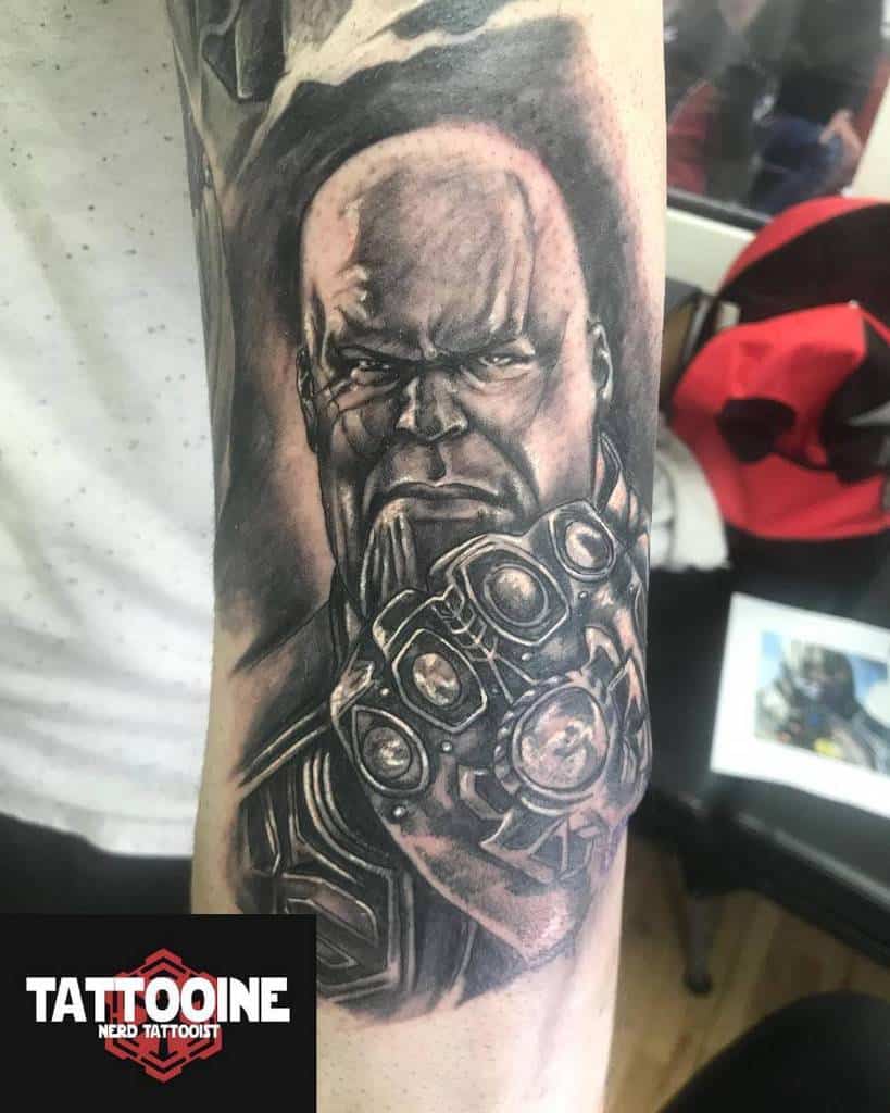 A black and gray tattoo of Thanos, showing his intense expression while holding the gauntlet with the Infinity Stones