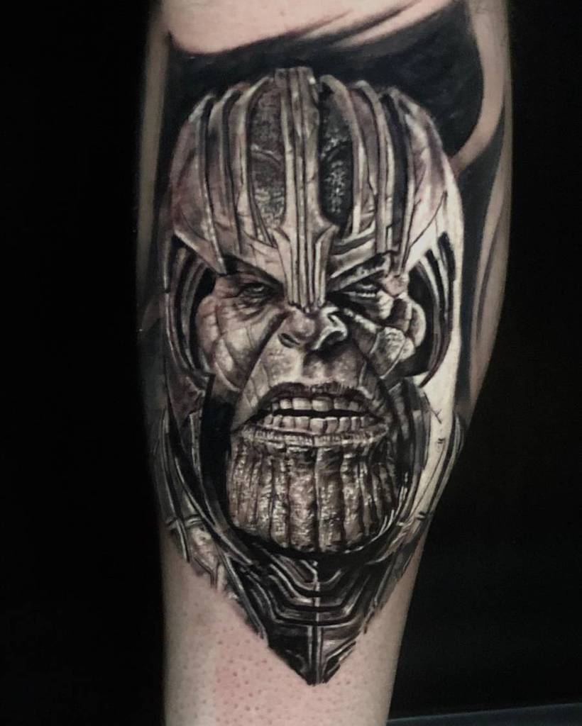 A black and gray tattoo of Thanos' face, showcasing a fierce expression with detailed shading and textures on his armor and facial features