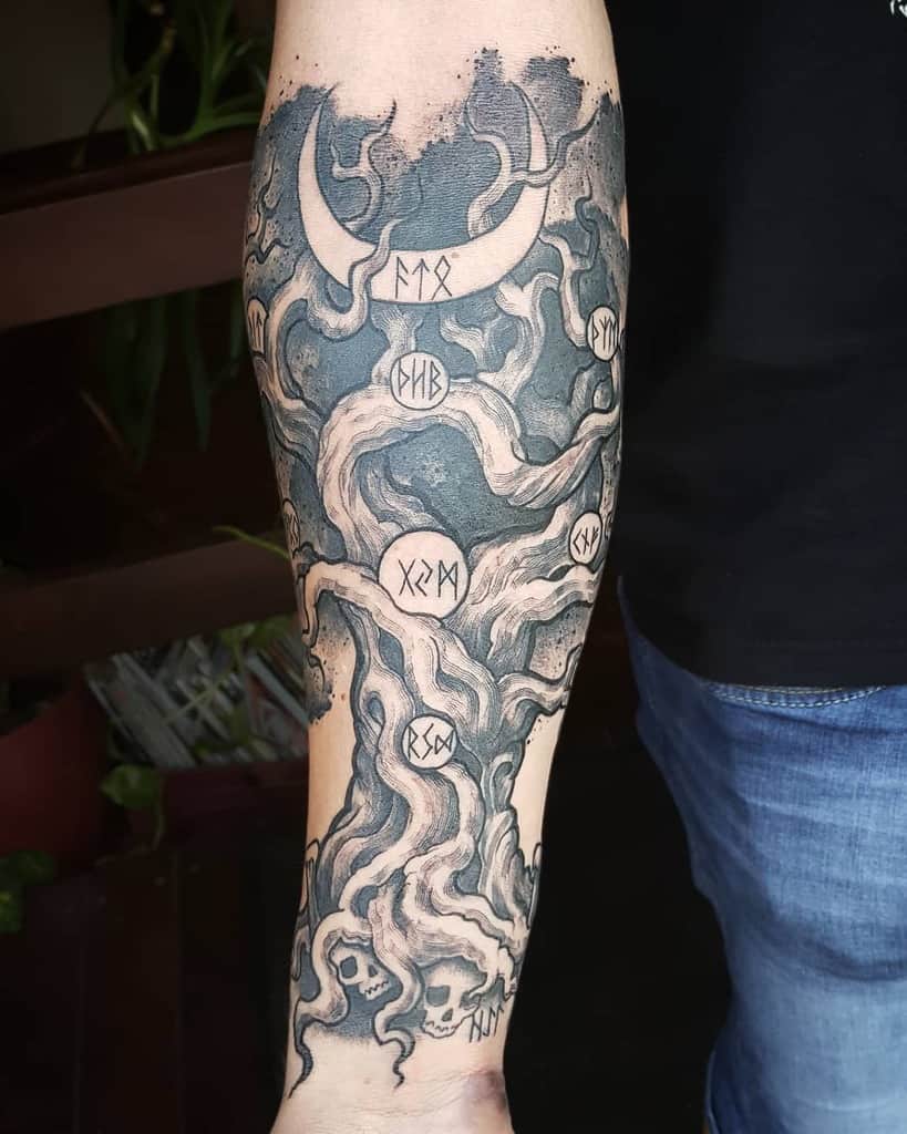 The tattoo features Yggdrasil with twisted branches, runes, a crescent moon, and skulls, blending Norse mythology with dark, mystical elements.