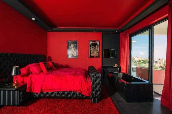 Red-themed bedroom with a cozy bed, vibrant art on the walls, and a scenic balcony view
