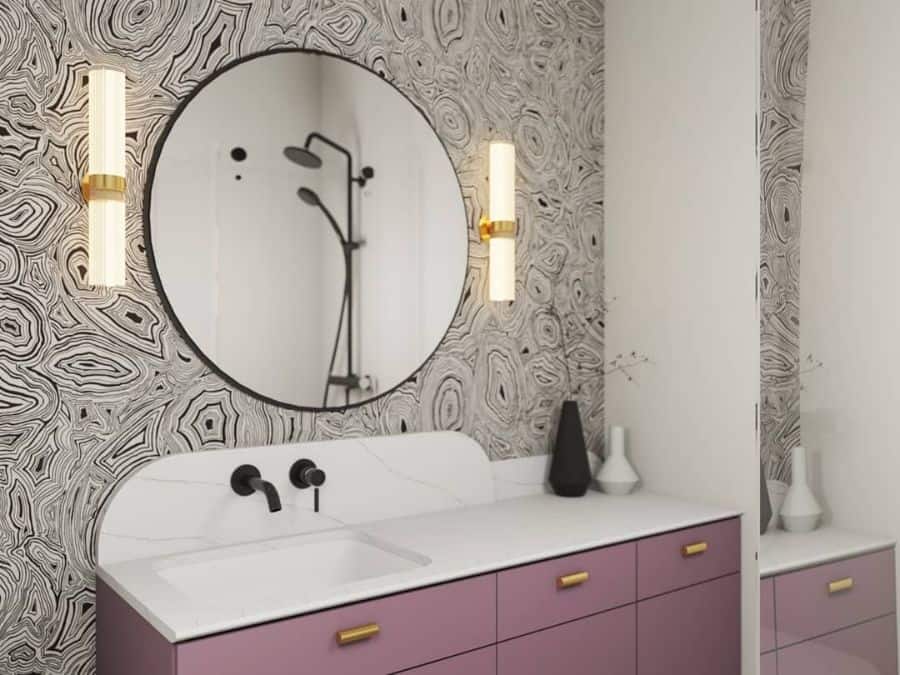 Bathroom with pink vanity, black and white patterned wallpaper, and round mirror.