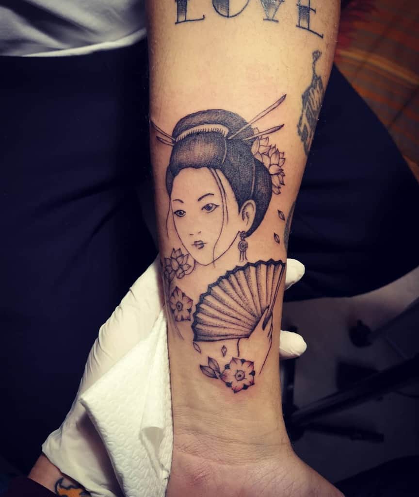 Black and gray forearm tattoo of a Geisha with an intricate hairstyle, holding a fan, surrounded by cherry blossoms and delicate linework.