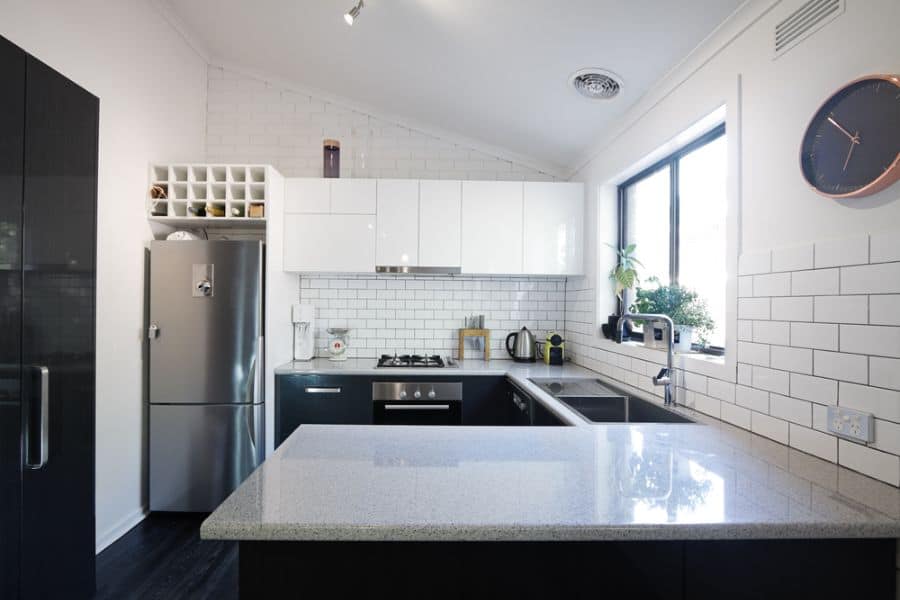 Compact black and white kitchen featuring white subway tile backsplash, glossy upper cabinets, and a sleek stone island countertop.