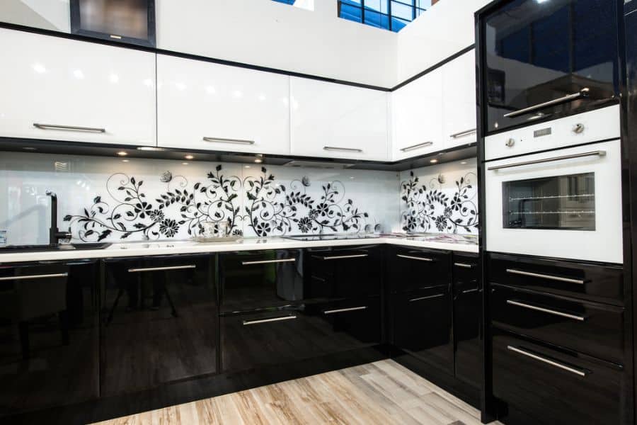 Modern kitchen with black and white cabinets, floral backsplash, and built-in oven.