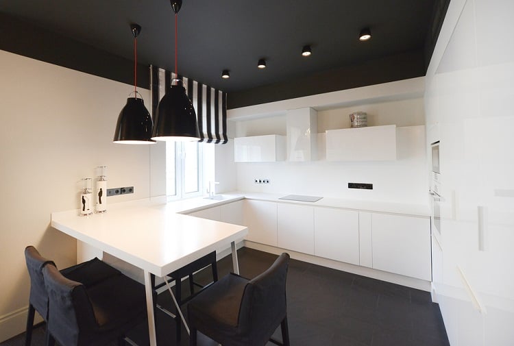 Modern kitchen with white cabinets, black ceiling featuring pendant lights, and a small dining table with black chairs