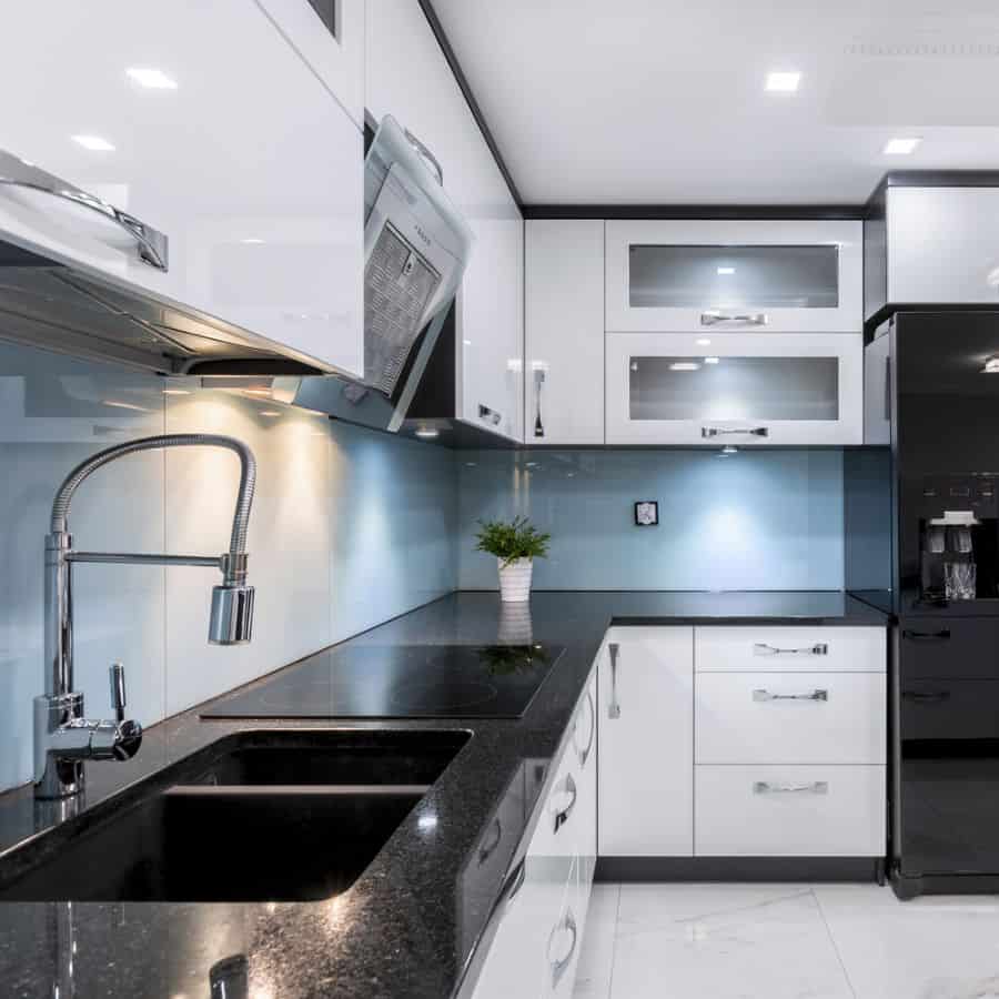 Modern kitchen with white cabinets, black countertops, and blue glass backsplash.