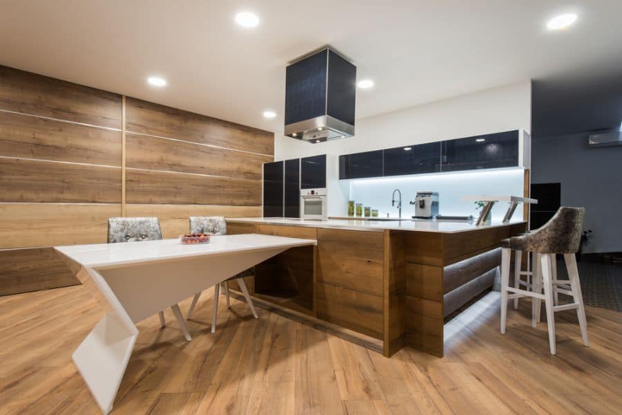 Modern kitchen with wood accents, black cabinets, white countertops, and unique dining table.